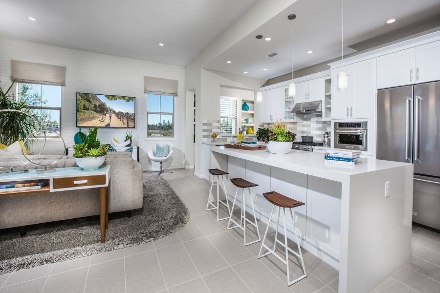 A kitchen and living area with pendant and recessed lighting, and raised window coverings.