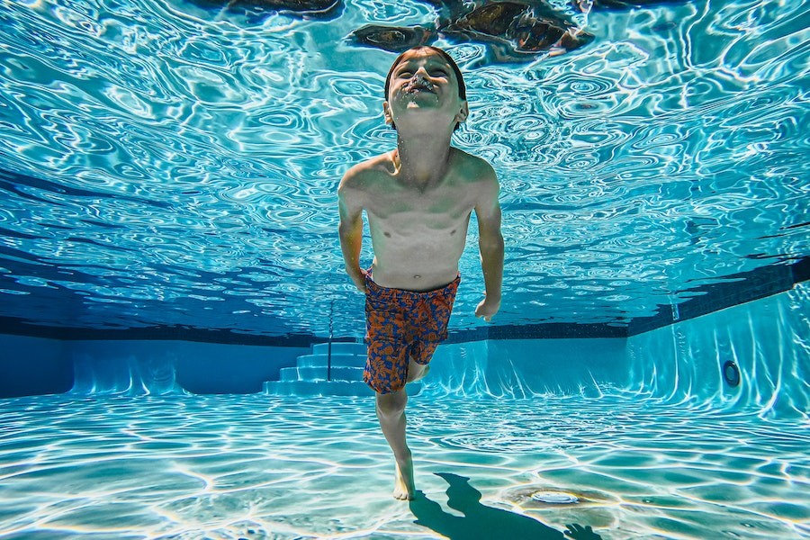 A boy happily swims underwater in a pool.
