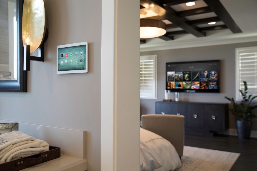 A wall with a Control4 touchscreen looking into a bedroom with a Control4 platform on the TV.