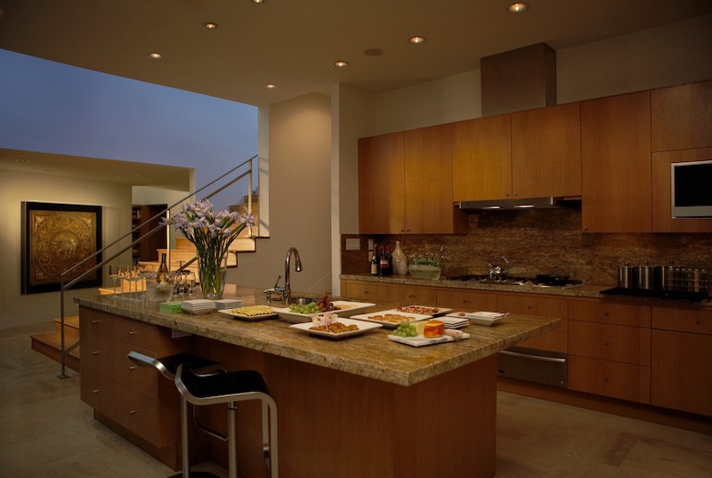 A warmly lit modern kitchen, with artwork in the background highlighted with soft lighting. 